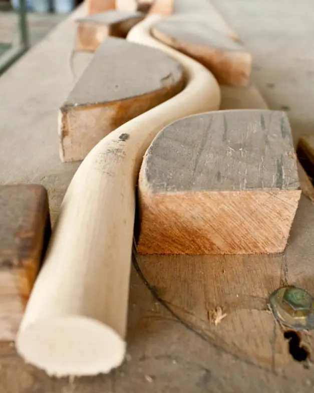 Close-up of a rattan rod being shaped with wooden molds at Vincent Sheppard factory, showing the craftsmanship behind frame production.