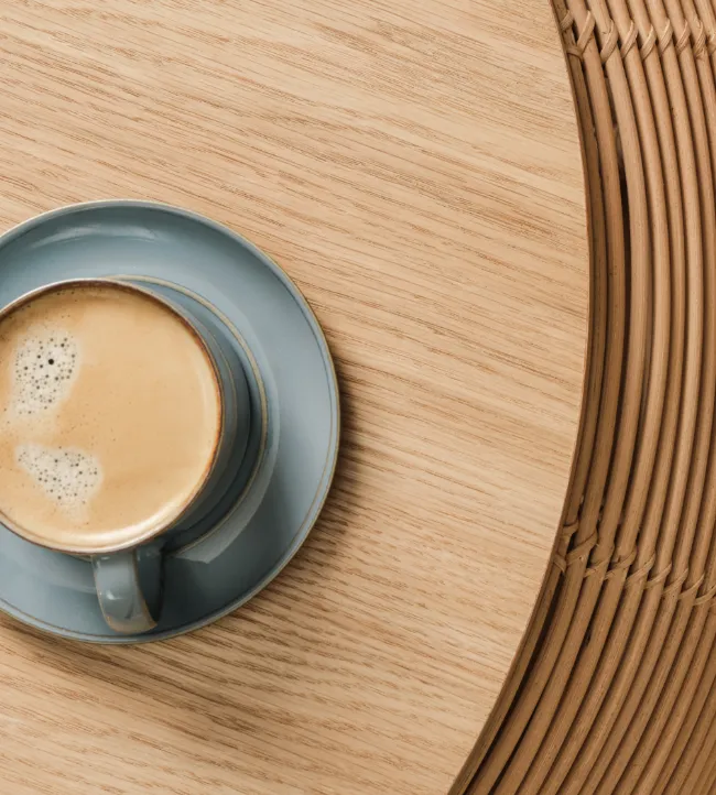 Vivi coffee table by Vincent Sheppard in natural oak, with a finely crafted rattan frame and a blue cup of coffee on top, set on a neutral rug.