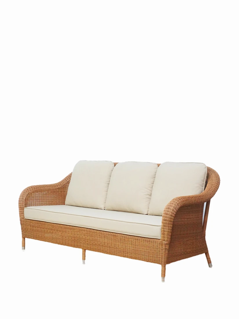 Angled view of the Riviera 3-seater sofa in honey synthetic wicker with beige cushions by Vincent Sheppard.