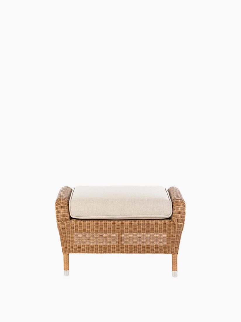 Front view of the Riviera ottoman in honey synthetic wicker with a beige cushion by Vincent Sheppard.