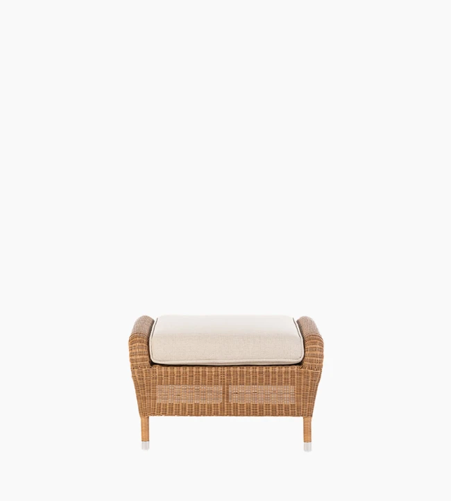 Front view of the Riviera ottoman in honey synthetic wicker with a beige cushion by Vincent Sheppard.