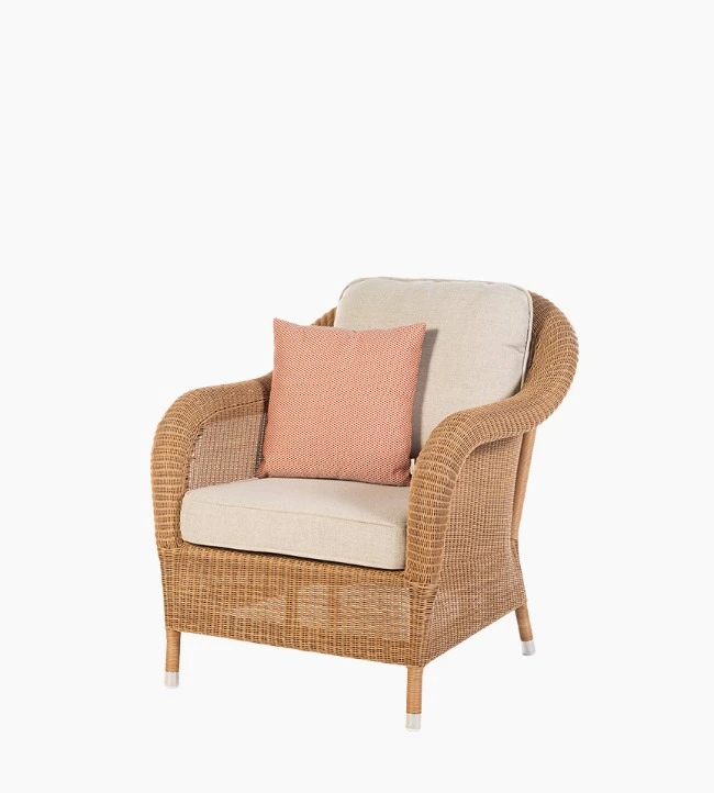 Vincent Sheppard’s Riviera armchair in honey synthetic wicker with beige cushions and a coral throw pillow.