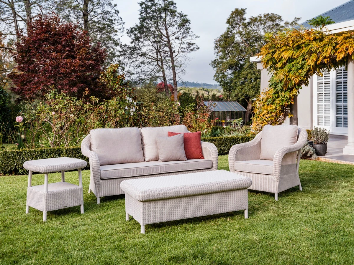 Vincent Sheppard Riviera Collection outdoor set featuring a sofa, armchair, ottoman, and side table woven in synthetic weave in Old Lace, arranged on a garden lawn.