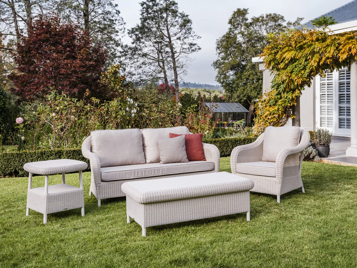 Vincent Sheppard Riviera Collection outdoor set featuring a sofa, armchair, ottoman, and side table woven in synthetic weave in Old Lace, arranged on a garden lawn.
