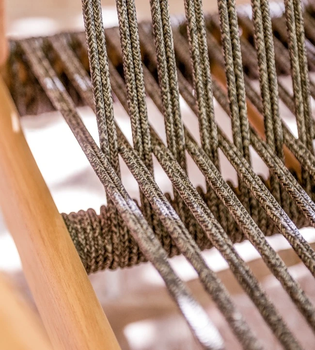 Close-up of a Vincent Sheppard chair featuring anthracite rope woven vertically across a warm teak wood frame. The braided rope adds texture and contrast to the smooth, natural finish of the teak, with sunlight enhancing the craftsmanship and material detail.