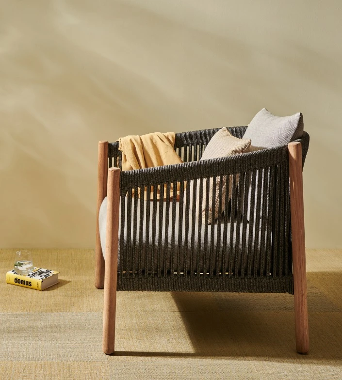 Lento Lounge Chair by Vincent Sheppard, with an anthracite rope frame, teak legs, and soft neutral cushions accented by a mustard throw. A calm, inviting composition that evokes relaxed elegance.