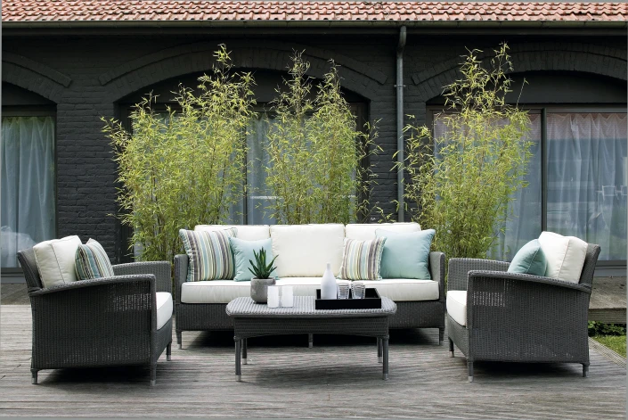 Dovile outdoor seating set by Vincent Sheppard, featuring a dark woven frame with white cushions and pastel accent pillows, arranged around a matching coffee table in a relaxed, contemporary garden setting.