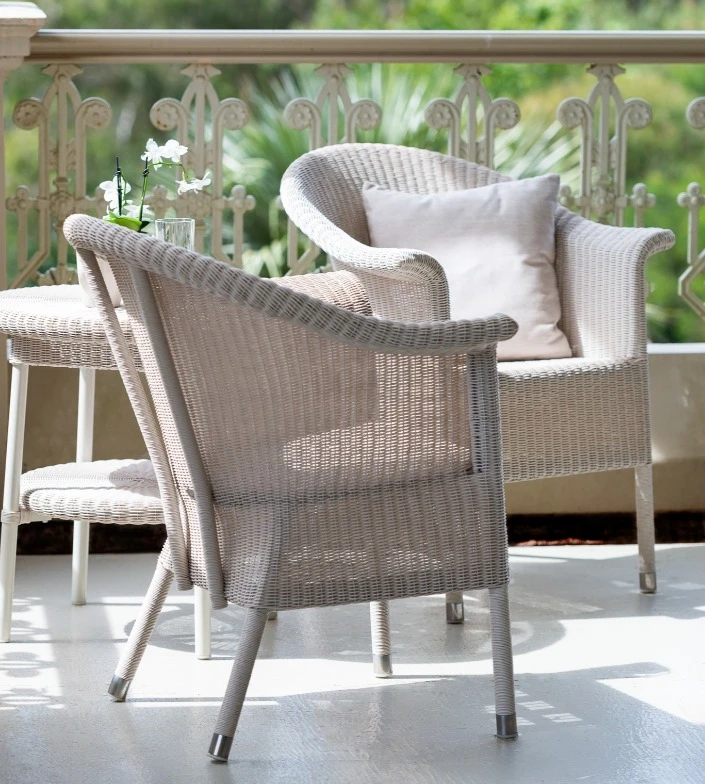Kenzo dining armchairs by Vincent Sheppard in Old Lace synthetic wicker, arranged on a sunlit veranda with decorative railing and lush greenery in the background.