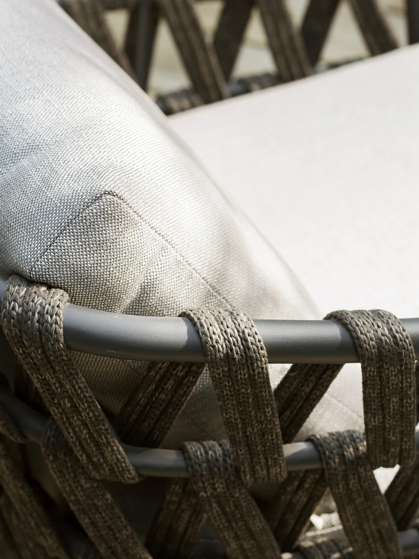 Close-up of the Leo Lounge Chair by Vincent Sheppard, featuring tightly woven dark rope around a matte frame and light grey Savane Zinc cushions with a textured fabric finish.