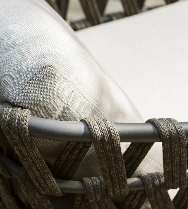 Close-up of the Leo Lounge Chair by Vincent Sheppard, featuring tightly woven dark rope around a matte frame and light grey Savane Zinc cushions with a textured fabric finish.