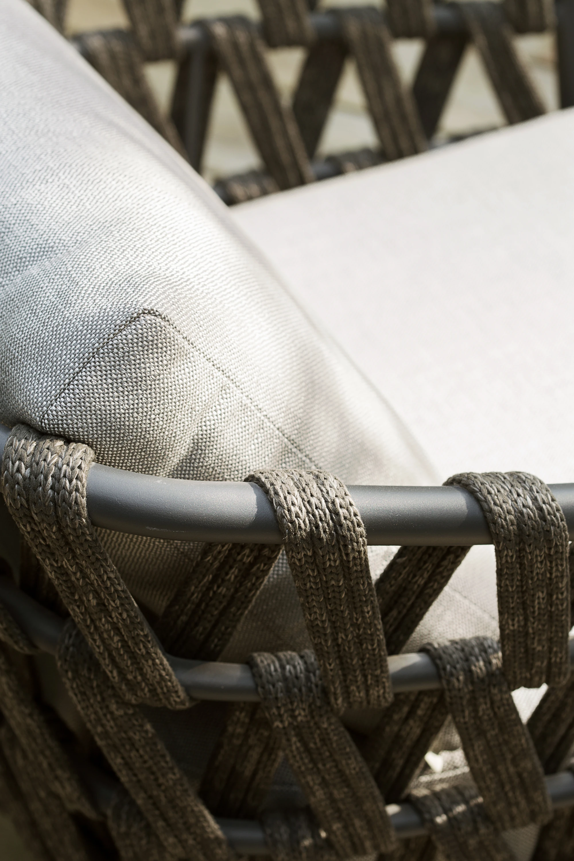 Close-up of the Leo Lounge Chair by Vincent Sheppard, featuring tightly woven dark rope around a matte frame and light grey Savane Zinc cushions with a textured fabric finish.