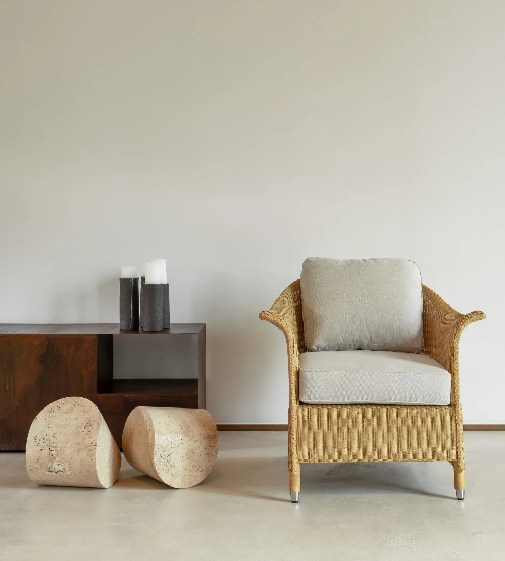 Victor Lounge Chair by Vincent Sheppard in a clear natural finish with plush Geneva Moon White cushions, positioned in a minimalist interior next to a low wooden console, cylindrical stone stools, and decorative vases.