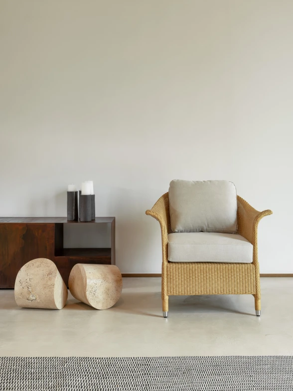 Victor Lounge Chair by Vincent Sheppard in a clear natural finish with plush Geneva Moon White cushions, positioned in a minimalist interior next to a low wooden console, cylindrical stone stools, and decorative vases.