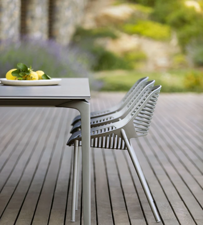 Allsize Table and Niwa chairs by FAST in  Iron Grey powder-coated aluminum, shown in an outdoor setting on a wooden deck with a natural garden backdrop.