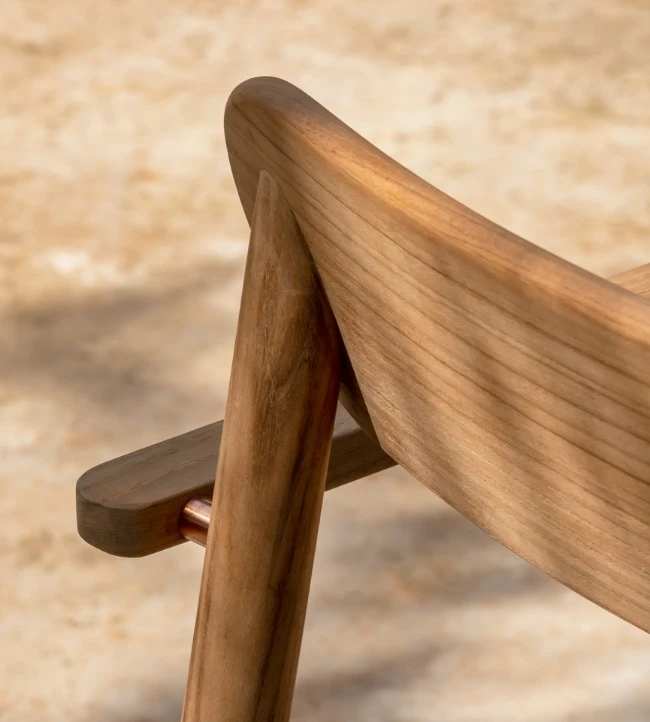Freya Dining Chair by Vincent Sheppard, highlighting the smooth curves and joinery of its teak wood frame with a gently angled backrest and slatted seat, bathed in dappled sunlight